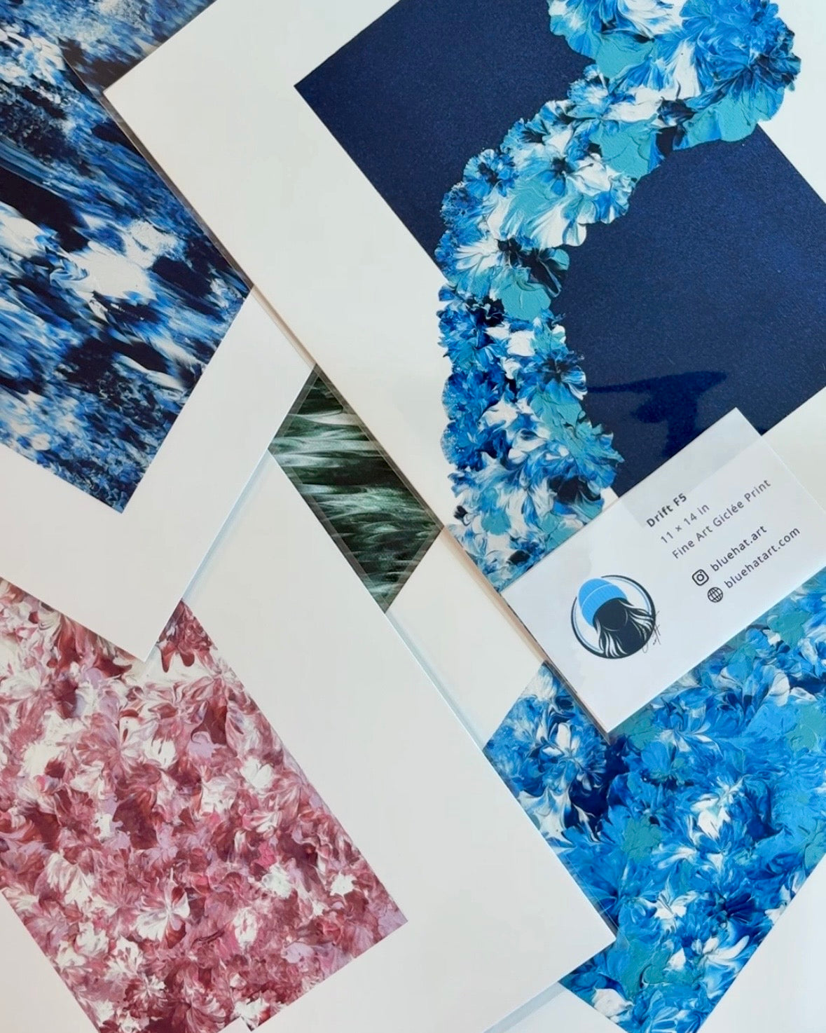 A framed abstract landscape painting featuring shades of blue, teal, and white, presented in a white frame with a wide white mat against a light beige textured wall.
