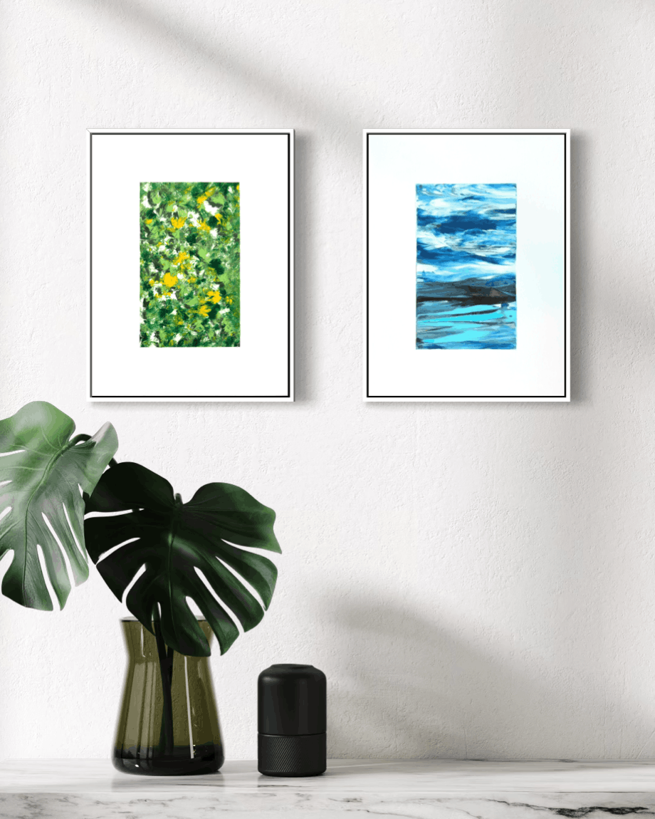 A framed art print featuring a green and yellow textured floral pattern, displayed on a white wall above a wooden table styled with a white vase of flowers, a vintage camera, and a small potted cactus.