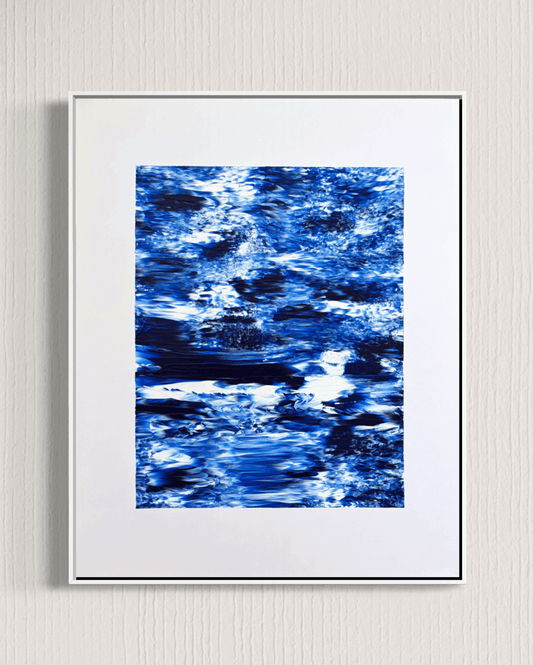 A framed abstract art print featuring a textured blue and white pattern resembling water ripples, presented in a white frame against a light gray textured wall.