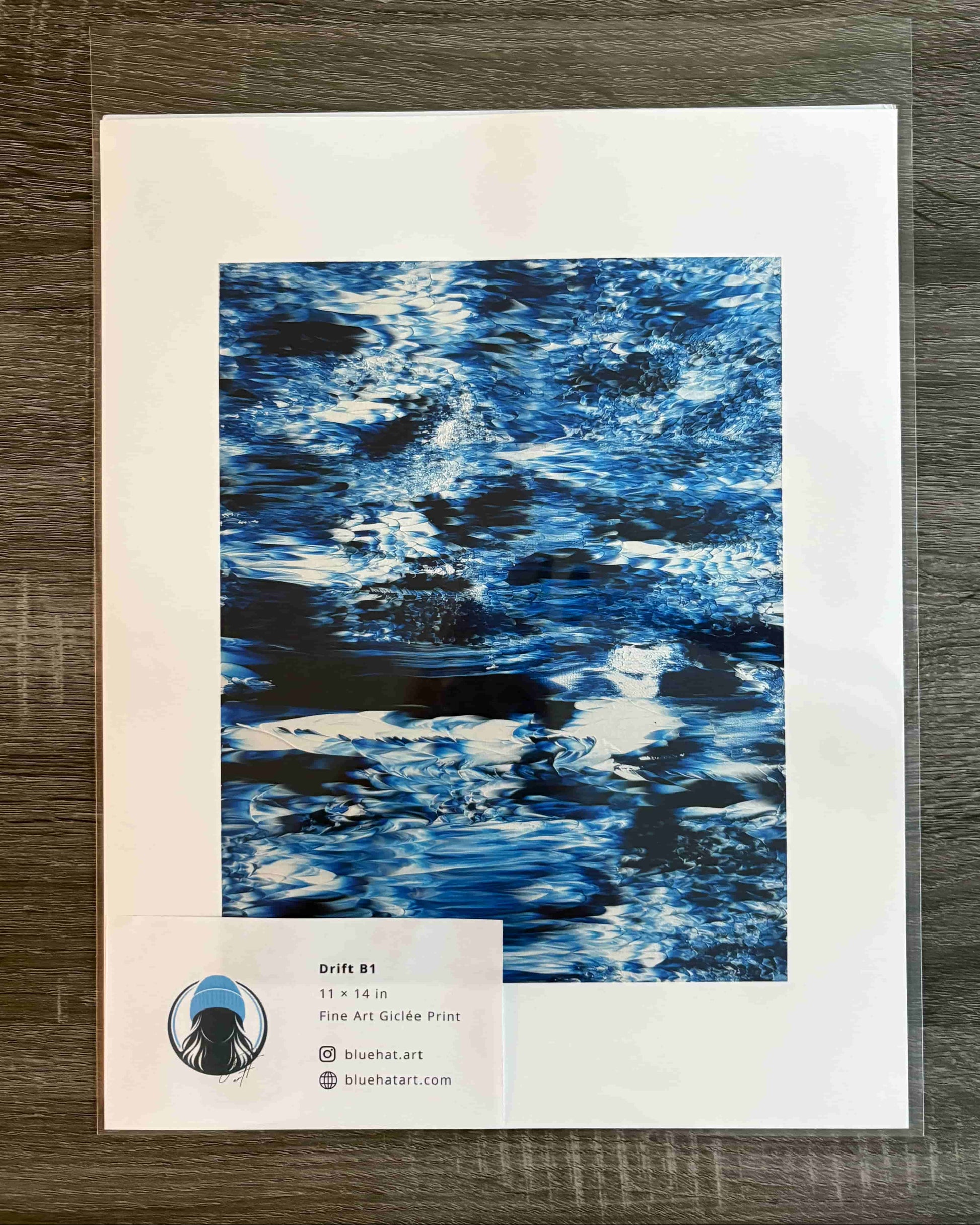 A framed or matted art print showing an abstract blue water-like pattern, placed on a dark wood surface. A small label at the bottom left reads 'Breeze 81' and 'Flow Art Gallery Print' with the website BreezeArt.
