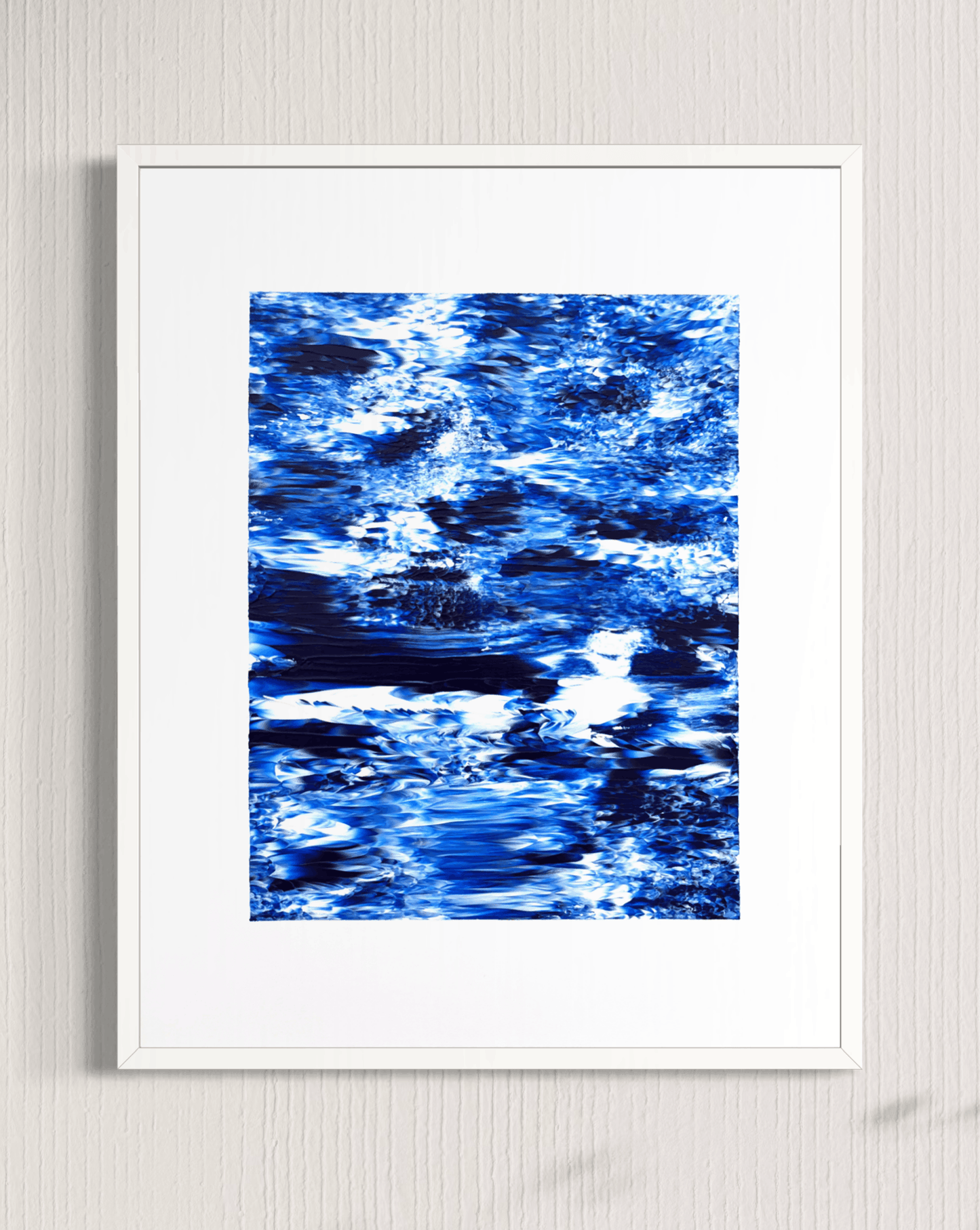 A framed abstract art print featuring a textured blue and white water-like pattern, presented in a white frame against a light gray textured wall.