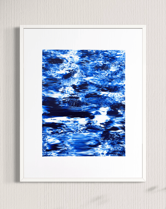 A framed abstract art print featuring a textured blue and white water-like pattern, presented in a white frame against a light gray textured wall.
