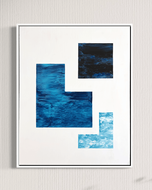 A framed abstract art print featuring three textured blue geometric blocks on a white background, enclosed in a thin black frame and hung on a light gray textured wall.