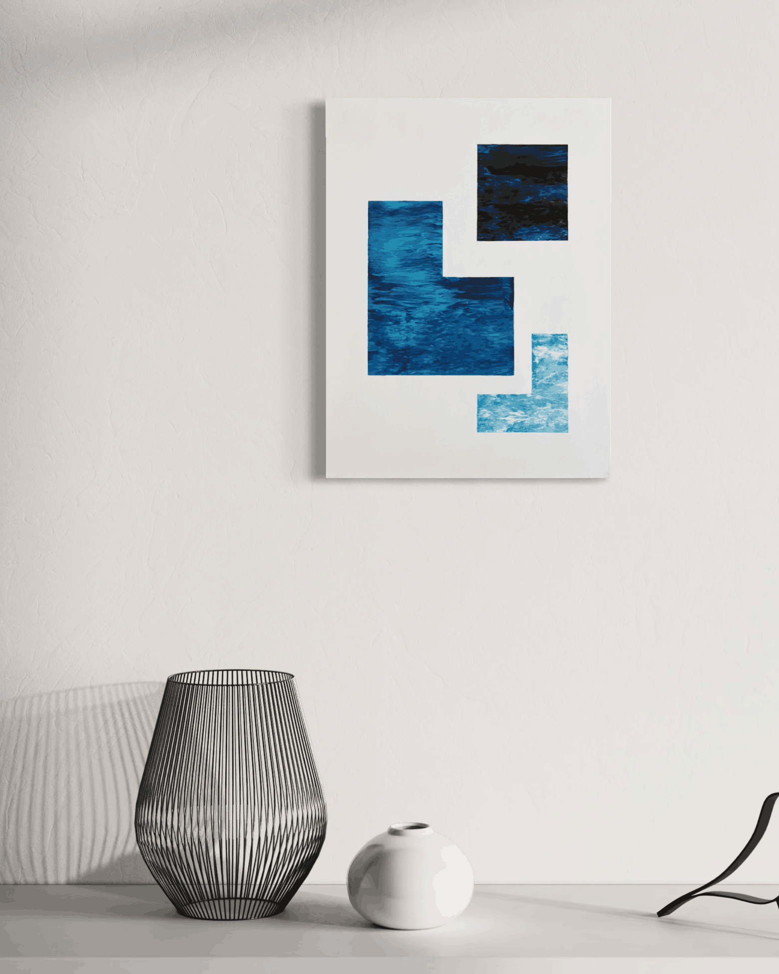 Abstract geometric wall art print featuring textured blue and black blocks on a white canvas, displayed on a white wall above a table with decorative vases.