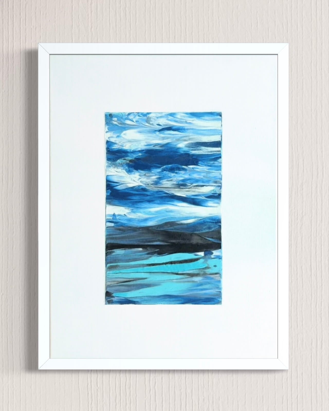 A framed abstract landscape painting featuring shades of blue, teal, and white, presented in a white frame with a wide white mat against a light beige textured wall.