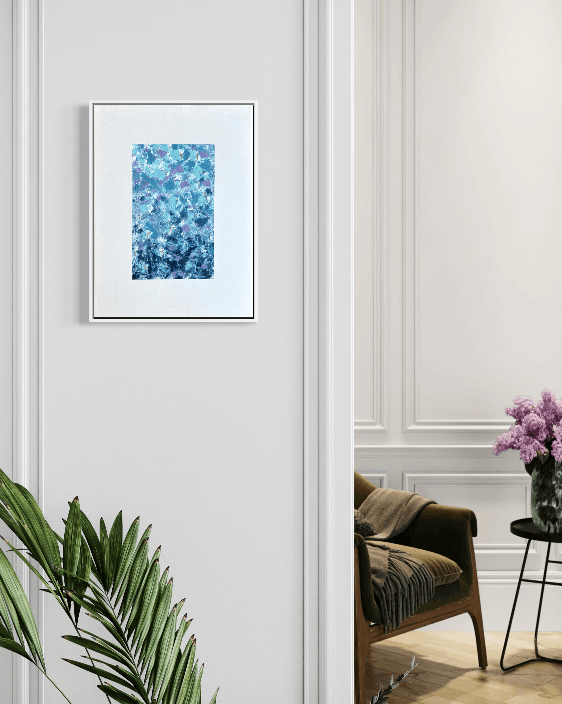 A framed abstract art print featuring a textured blue and teal floral pattern, displayed on a white paneled wall in a styled interior room with a green armchair and a plant.