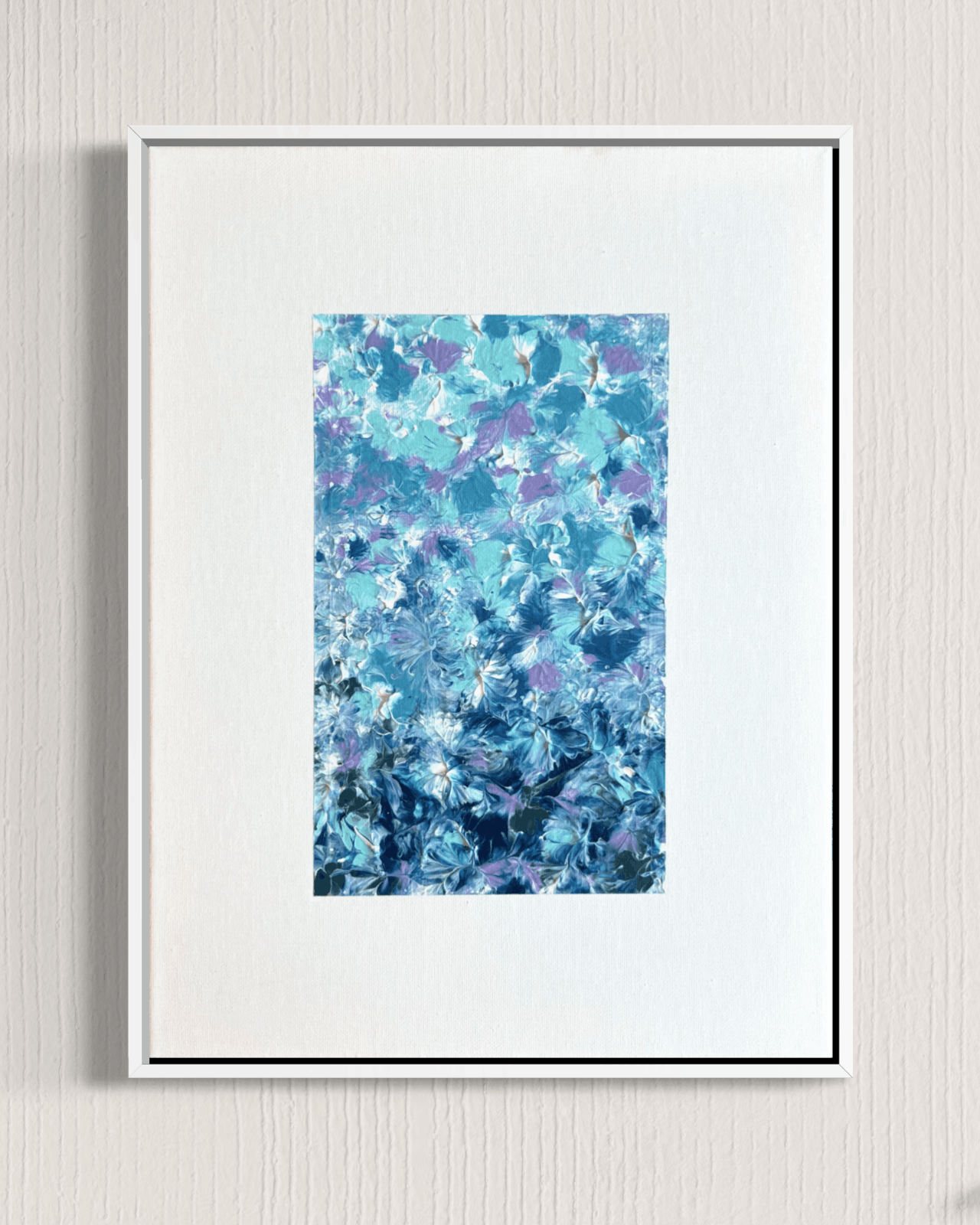 A framed abstract art print featuring a textured pattern of blue, teal, and purple brushstrokes, presented in a white frame with a wide white mat against a light gray textured wall.