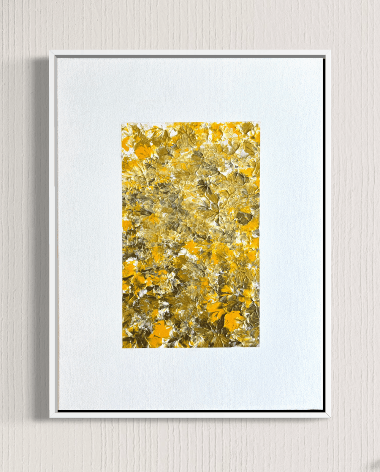 A framed abstract art print featuring a textured pattern of yellow, gold, and white brushstrokes, presented in a white frame with a white mat against a light gray textured wall.