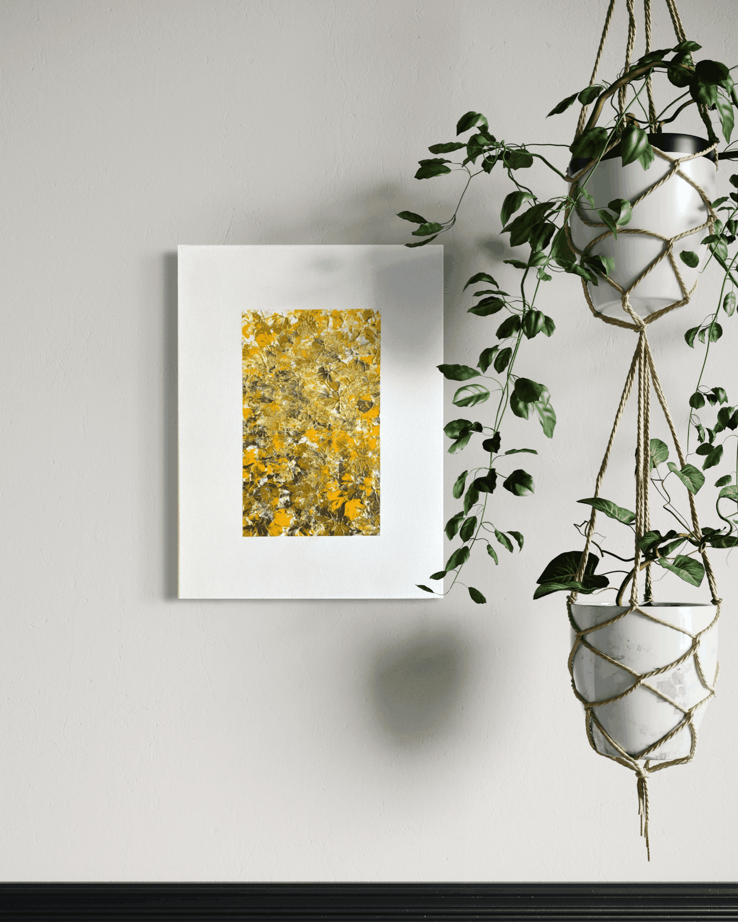 A framed abstract art print featuring a textured yellow and gold floral pattern, displayed on a light gray wall next to hanging green houseplants.