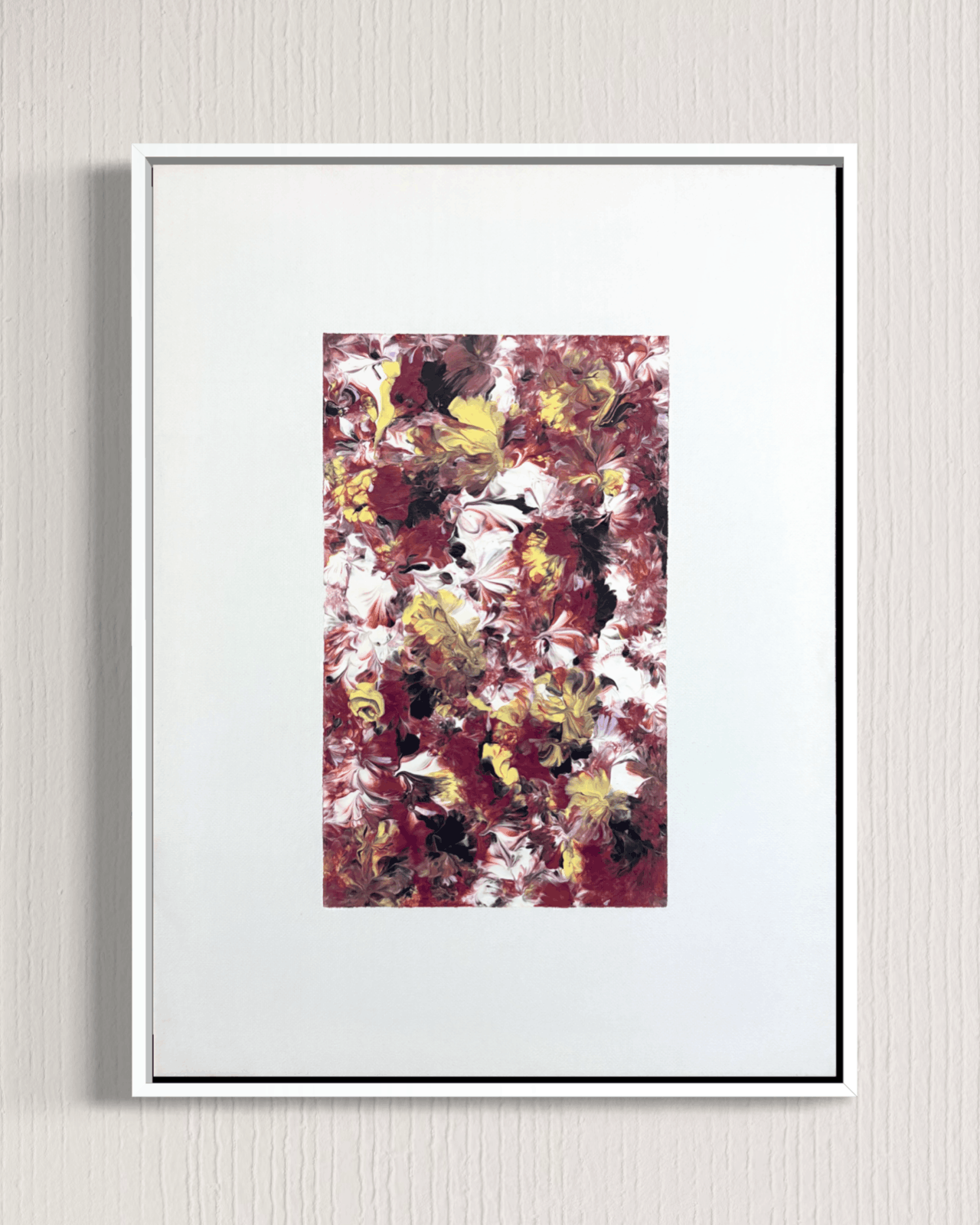 A framed abstract art print featuring a textured floral pattern in burgundy, white, yellow, and black, presented in a white frame against a light gray textured wall.