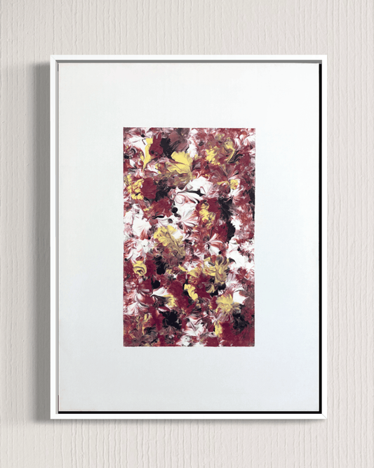 A framed abstract art print featuring a textured floral pattern in burgundy, white, yellow, and black, presented in a white frame against a light gray textured wall.