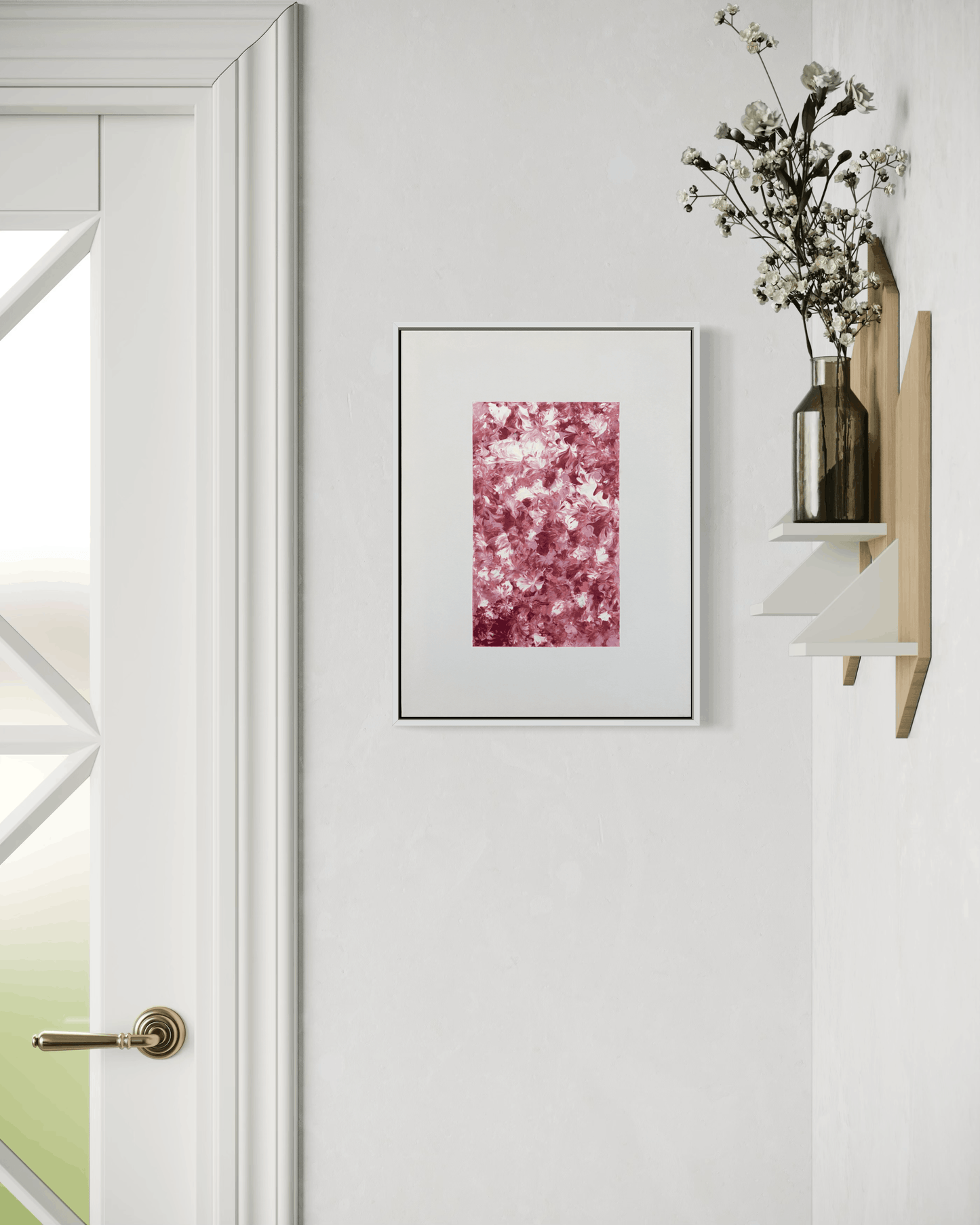 A framed abstract art print with a pink and burgundy floral pattern, displayed on a white wall next to a wooden shelf holding a glass vase with dried white flowers.
