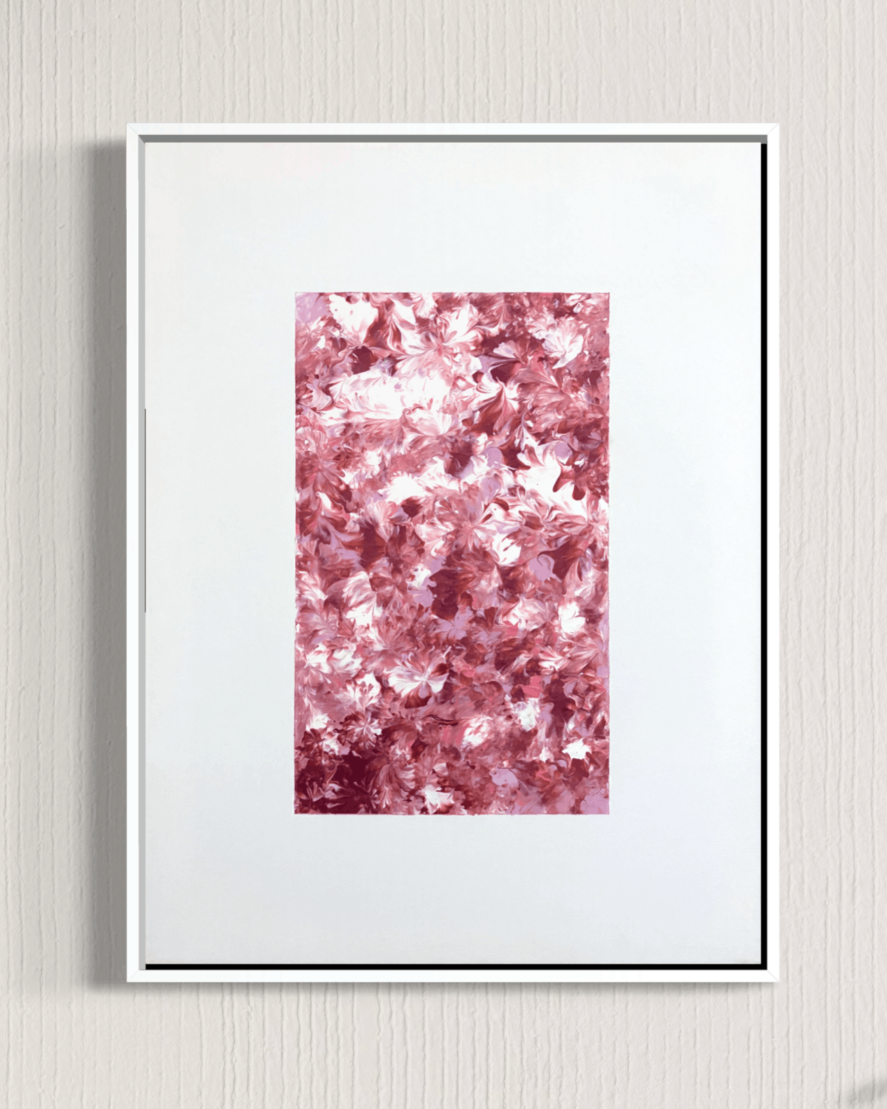A framed abstract art print featuring a textured field of pink and white floral-like shapes, presented in a white frame against a light gray textured wall.