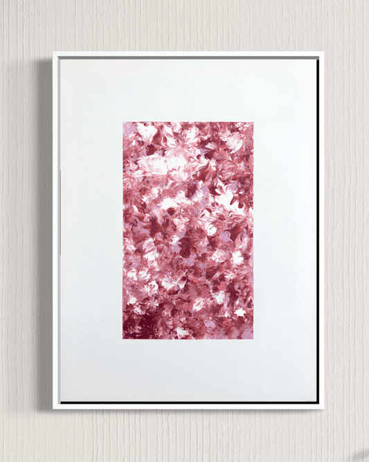 A framed abstract art print featuring a textured field of pink and white floral-like shapes, presented in a white frame against a light gray textured wall.