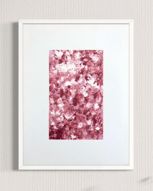 A framed abstract art print featuring a textured, glittery pink and rose gold pattern in the center, surrounded by a wide white mat and a clean white frame, mounted on a light gray textured wall.
