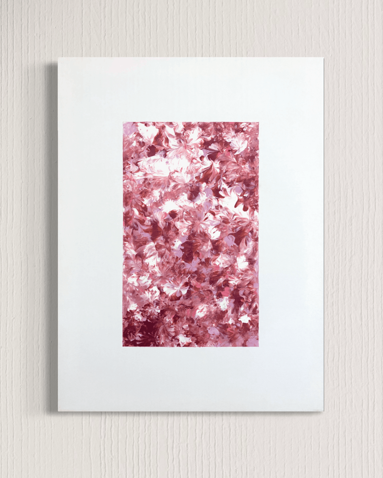 A framed wall art print featuring a central rectangular panel filled with dense pink and rose-gold floral or leaf-like texture, surrounded by a wide white mat on a light neutral wall.