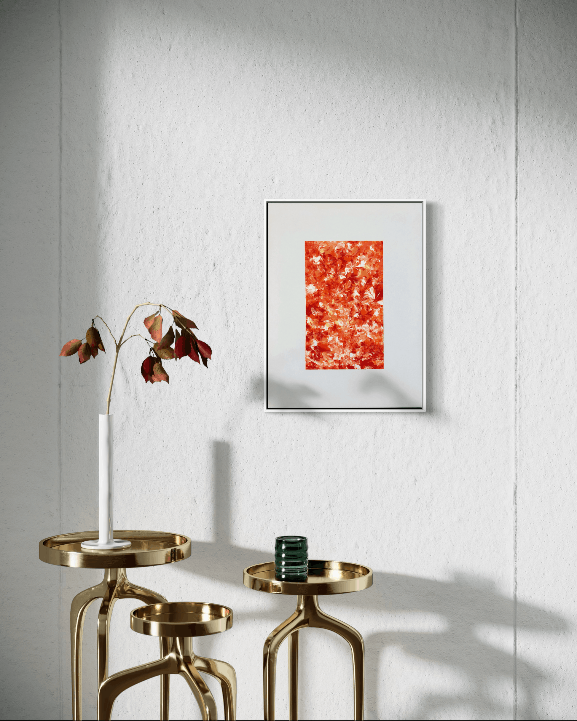 A framed abstract art print with a vibrant orange and red textured design hangs on a white textured wall above two gold side tables with a white vase and a small green cup.
