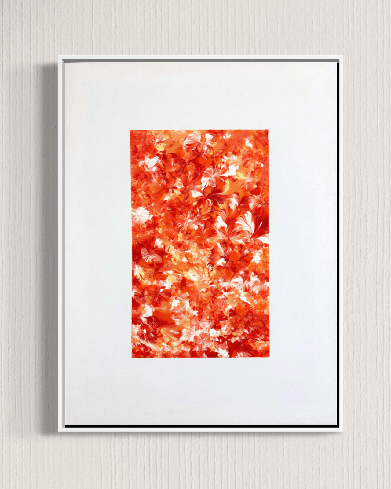 A framed abstract art print featuring a textured pattern of orange, red, and white leaf-like shapes, presented in a white frame against a light gray textured wall.