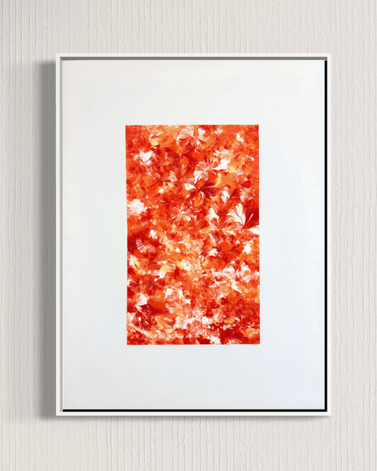 A framed abstract art print featuring a textured pattern of orange, red, and white leaf-like shapes, presented in a white frame against a light gray textured wall.