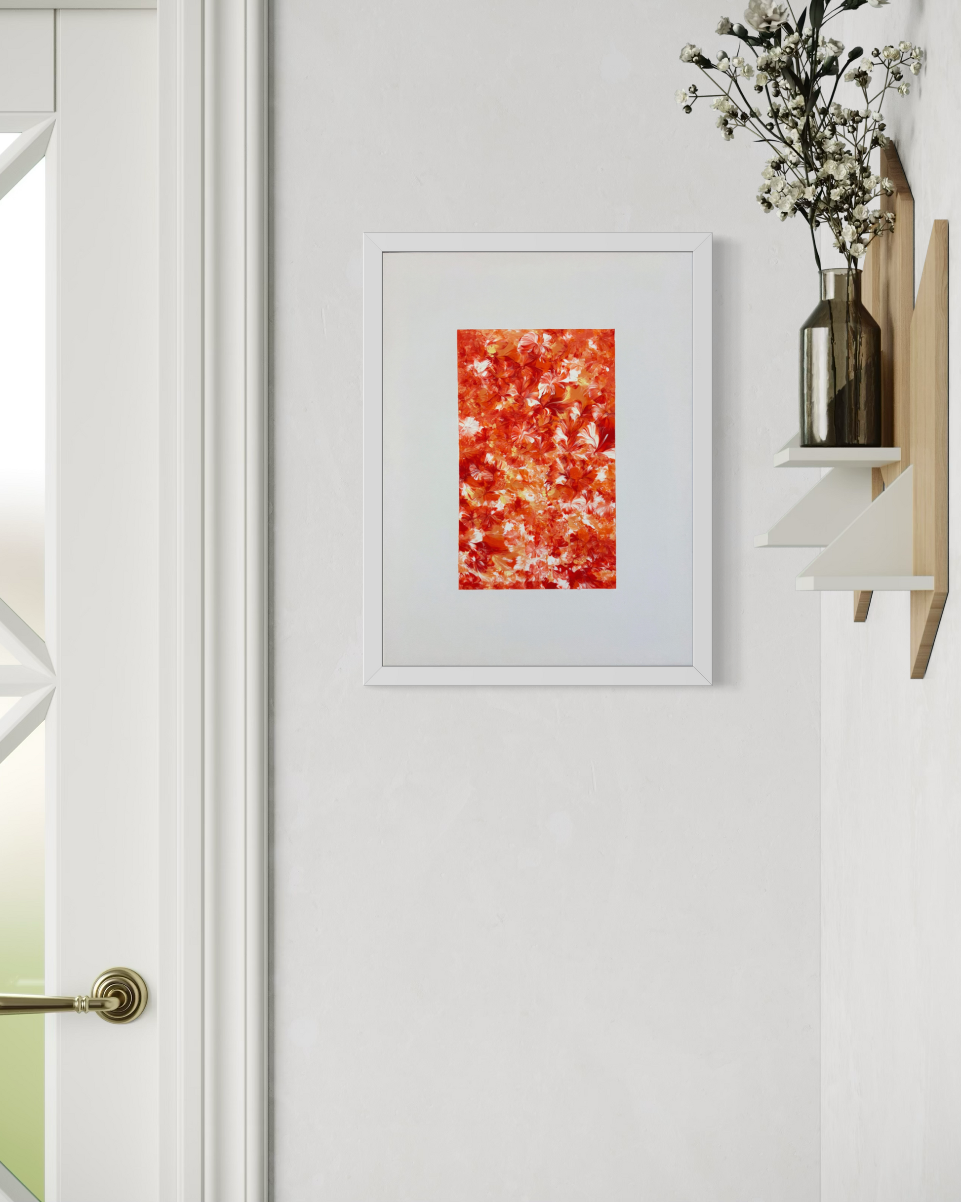 A framed abstract art print featuring a vibrant red and orange textured pattern with white highlights, displayed on a clean white wall next to a shelf with dried flowers.