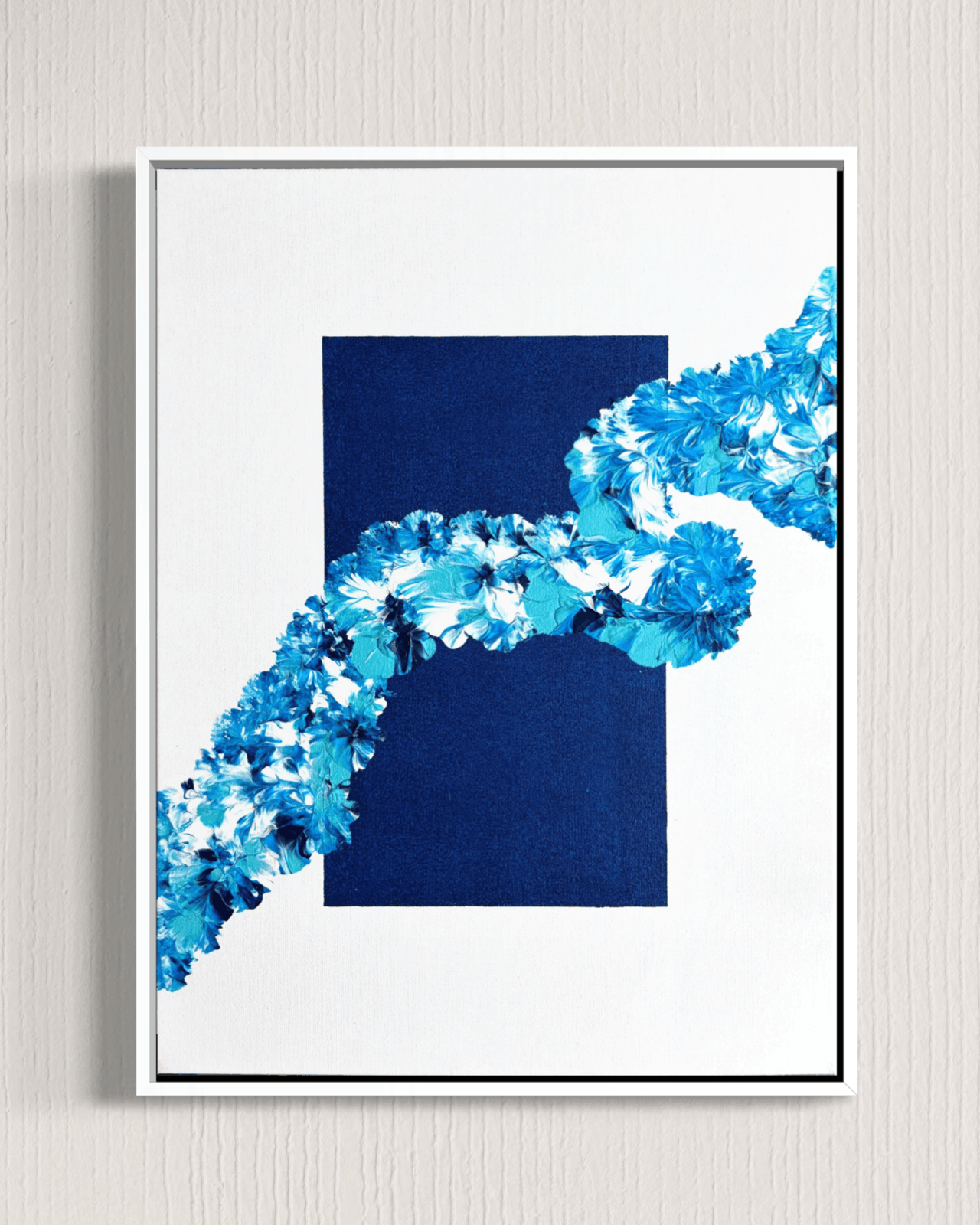 A framed abstract art print featuring a dark navy blue rectangle and a diagonal wave-like pattern of textured blue and white flowers, set against a light gray textured wall.