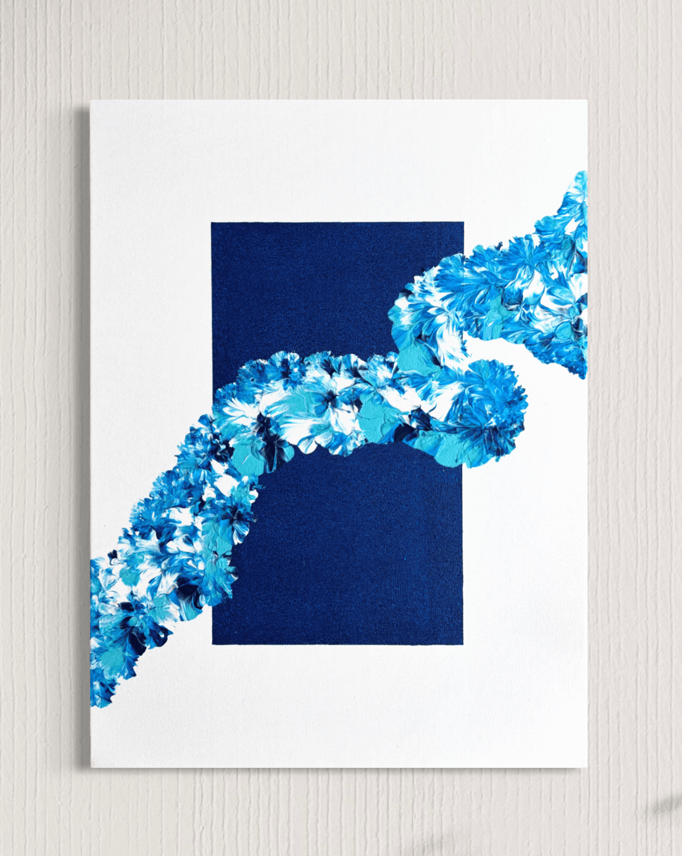 An abstract art print featuring a dark navy blue rectangle and a diagonal blue floral pattern on a white background, shown hanging on a light gray textured wall.