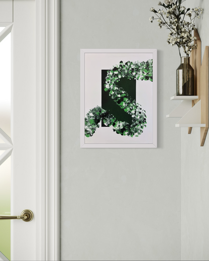 A framed abstract art print featuring a green and white leafy spiral design on a white background, displayed on a light gray wall next to a white door frame and a wooden shelf with a vase of flowers.