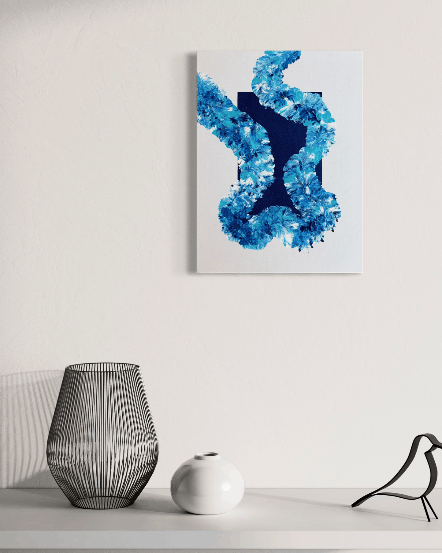 Abstract canvas wall art featuring a textured blue and navy blue design on a white background, displayed on a wall above a shelf with decorative objects.