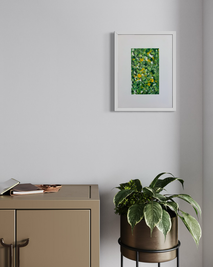 A framed abstract green and yellow painting hangs on a light gray wall above a beige cabinet, with a potted plant on a black metal stand nearby.