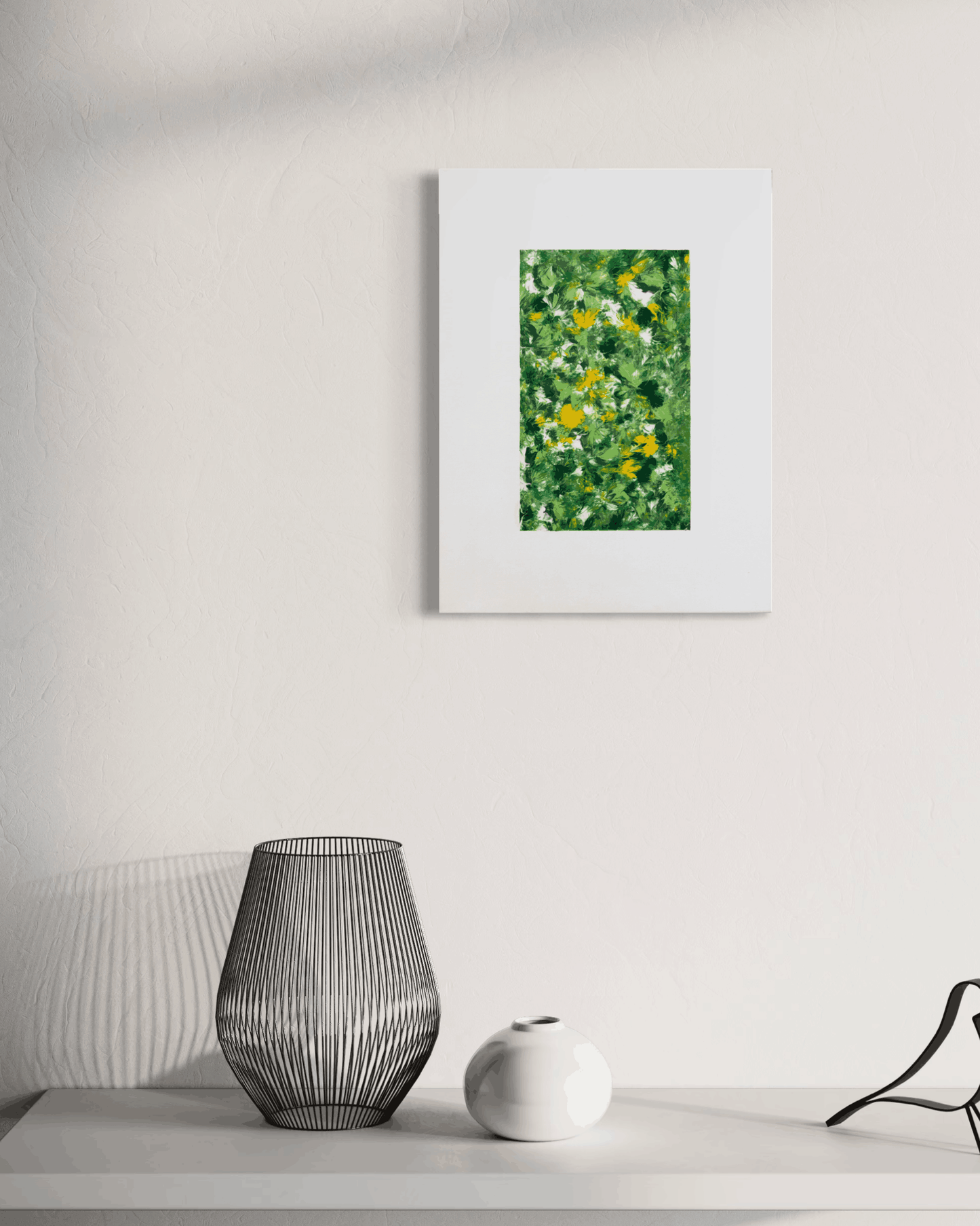A framed art print featuring a green and yellow floral pattern, displayed on a white wall above a shelf with decorative objects.