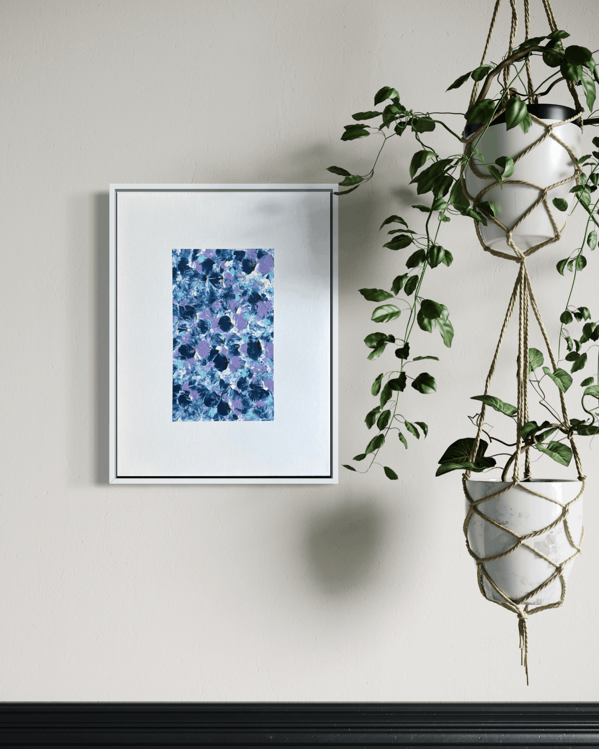 A framed abstract art print featuring blue and purple floral patterns, displayed on a light beige wall next to a hanging green plant in a white geometric pot.