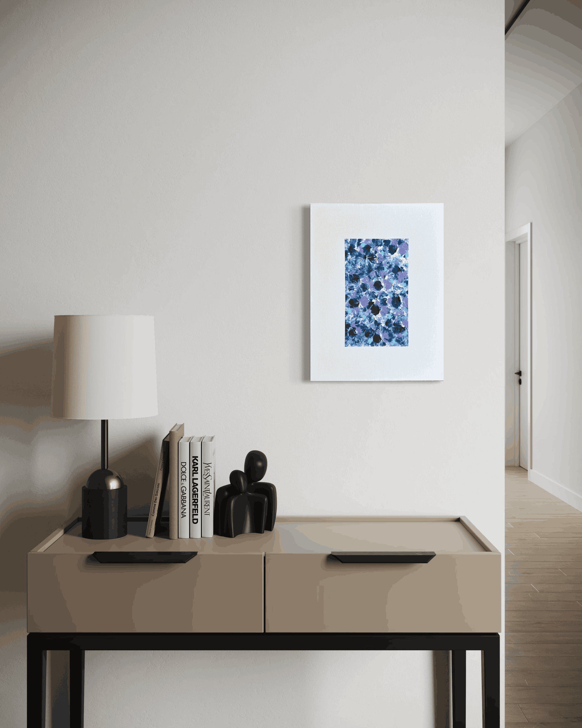 A framed abstract art print featuring a blue and white floral pattern, displayed on a light beige wall above a modern console table with a lamp and books.