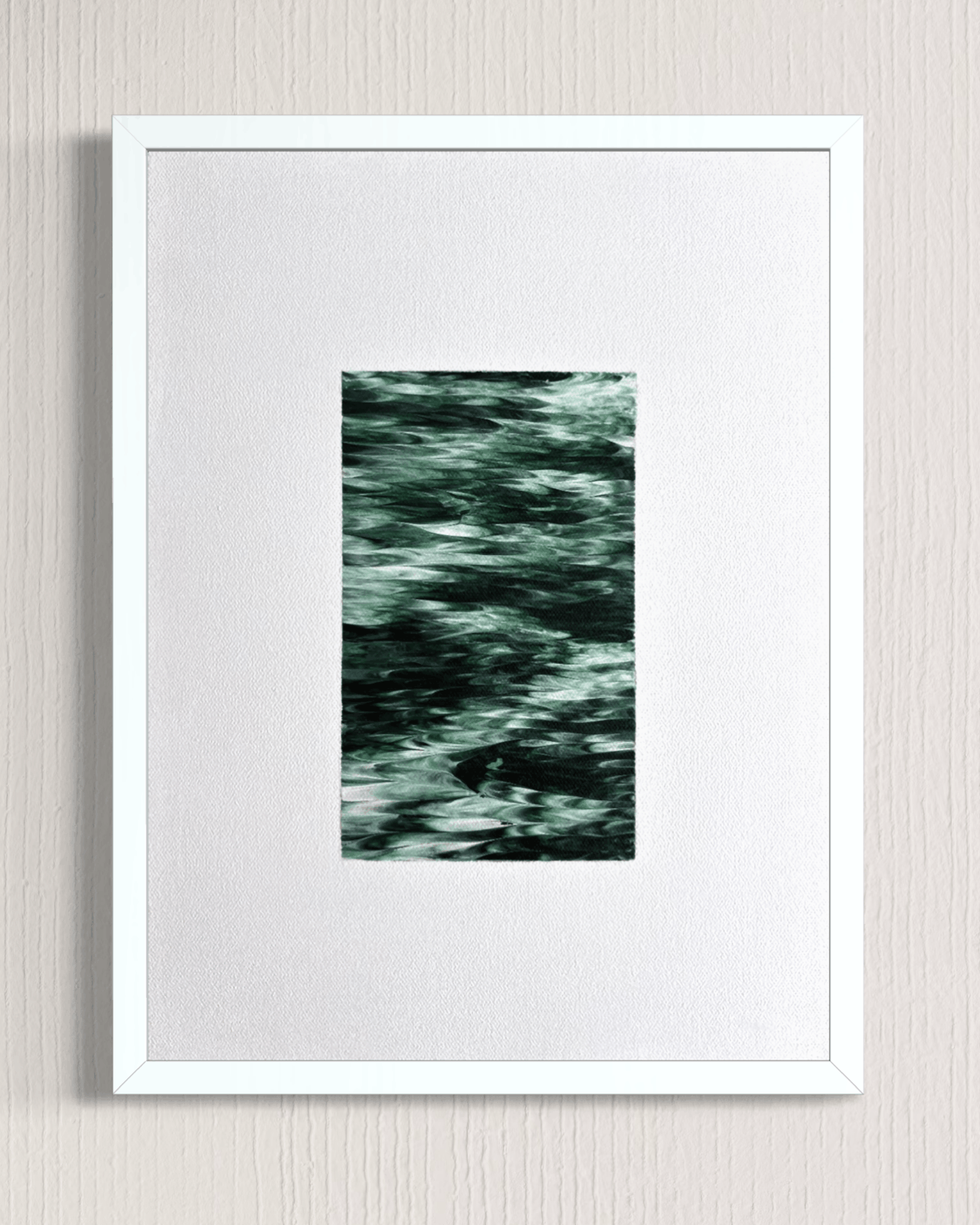 A framed abstract art print featuring a textured, dark green and black pattern in the center, surrounded by a wide white mat and a simple white frame, mounted on a light gray textured wall.