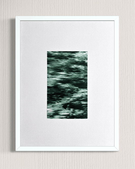 A framed abstract art print featuring a textured, dark green and black pattern in the center, surrounded by a wide white mat and a simple white frame, mounted on a light gray textured wall.