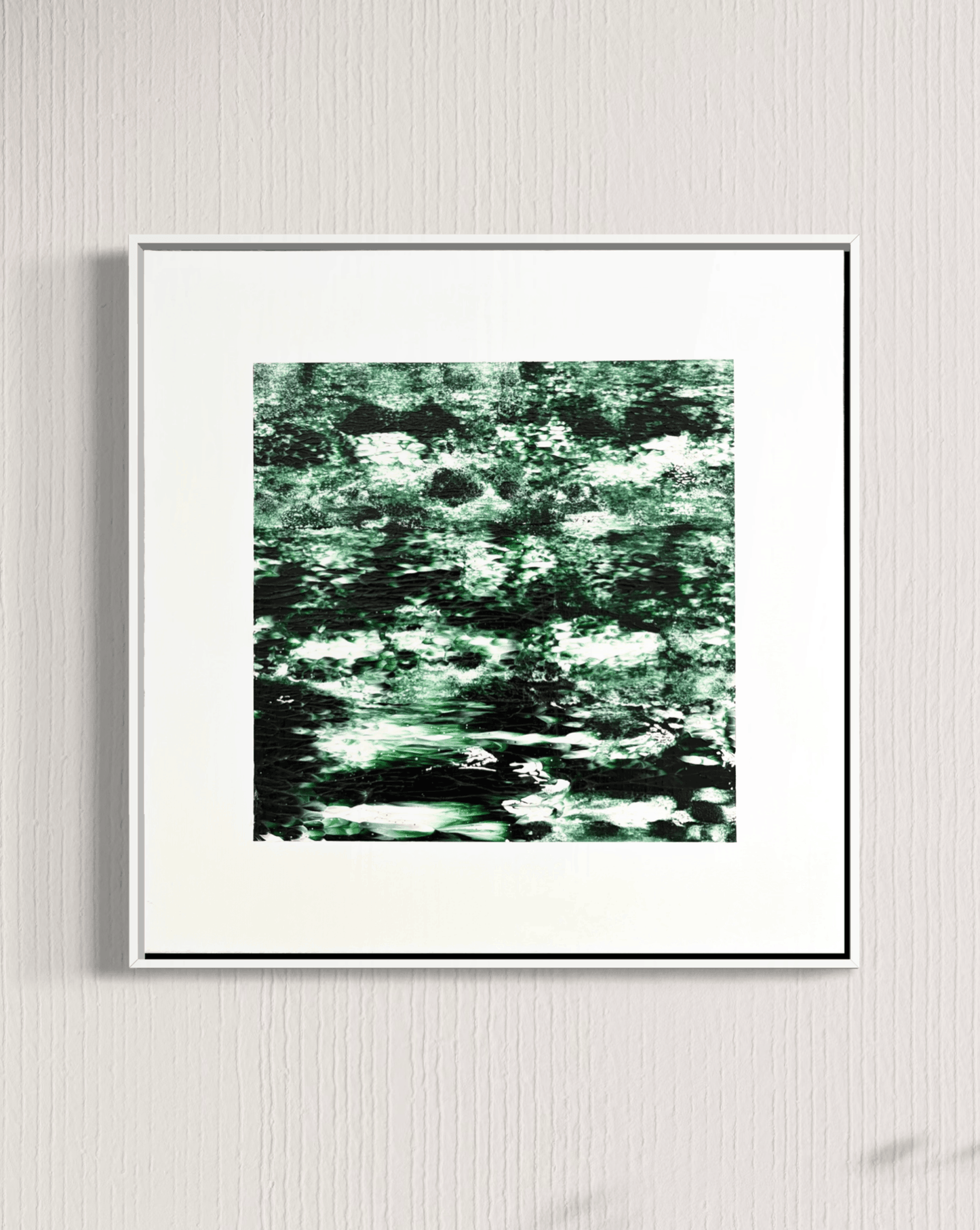 A framed abstract art print featuring a textured pattern of green, black, and white brushstrokes, displayed on a light gray textured wall.