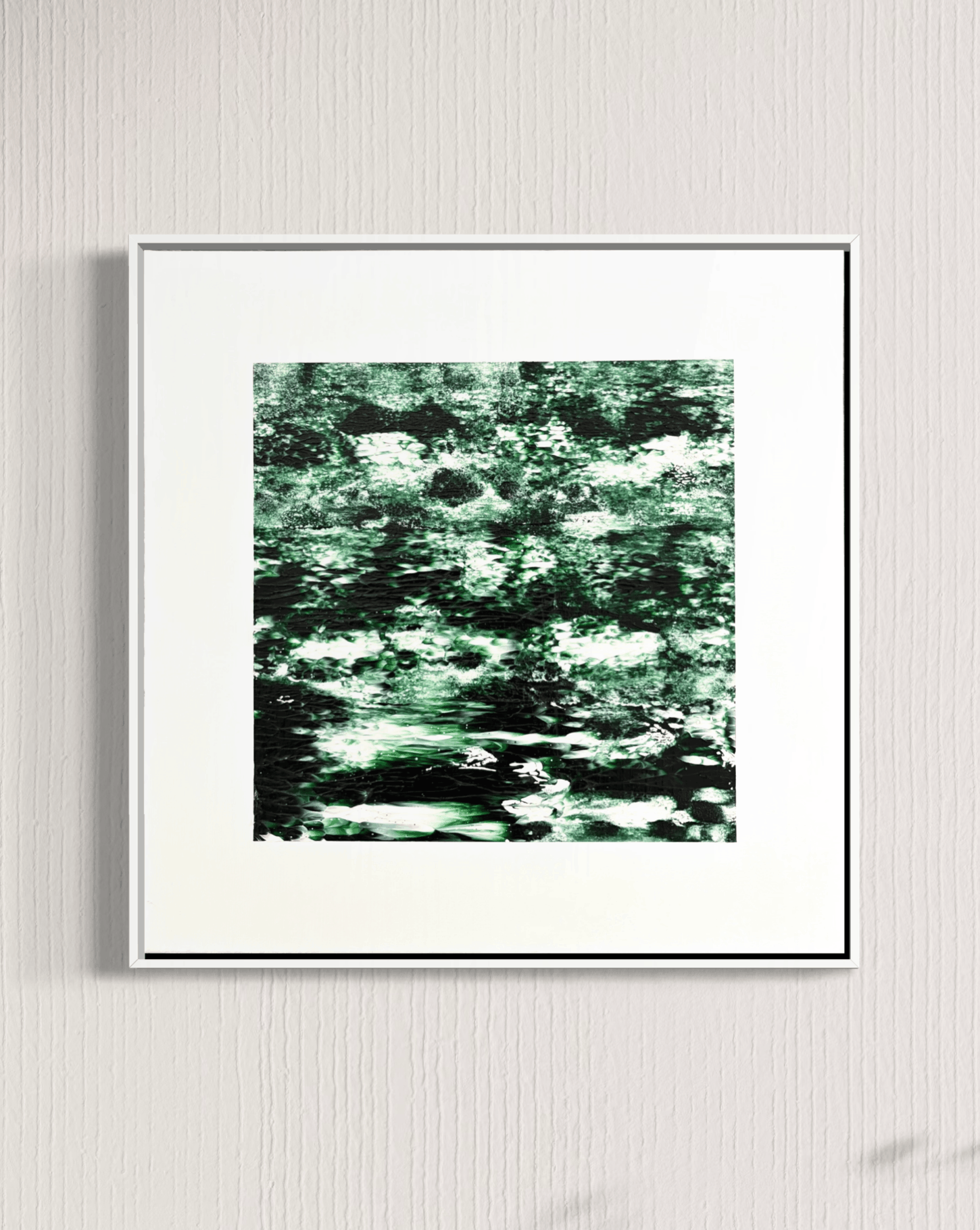 A framed abstract art print featuring a textured pattern of green, black, and white brushstrokes, displayed on a light gray textured wall.