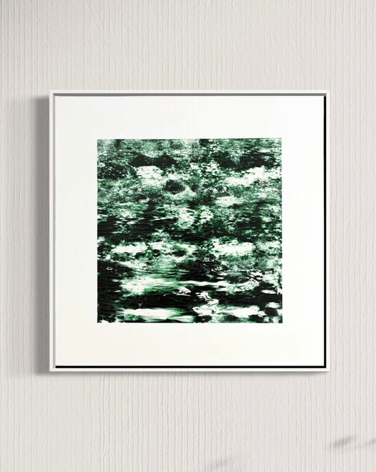 A framed abstract art print featuring a textured pattern of green, black, and white brushstrokes, displayed on a light gray textured wall.
