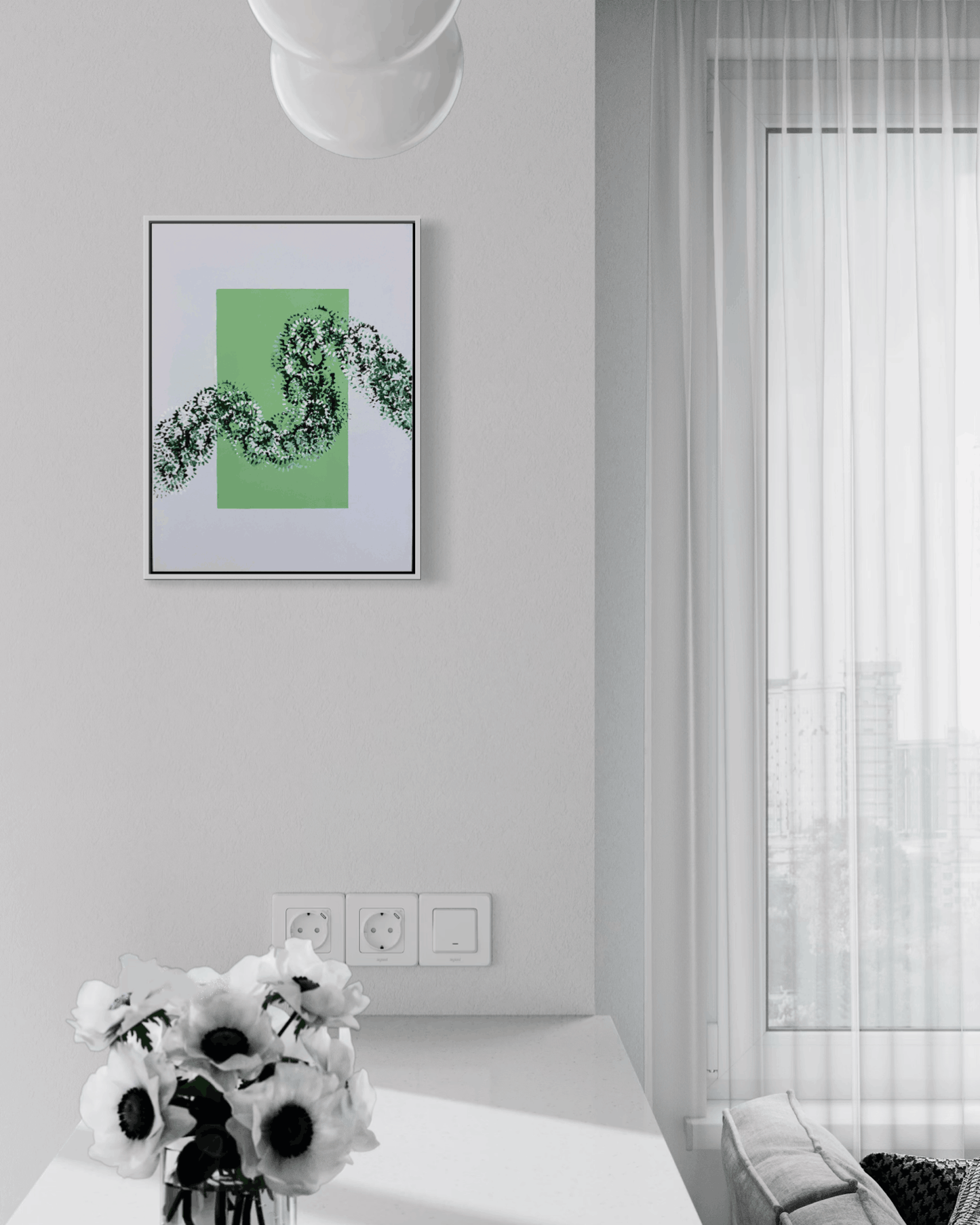 A framed abstract art print featuring a green square and black floral line art, hanging on a light gray wall in a modern, sunlit room with a window and white curtains.