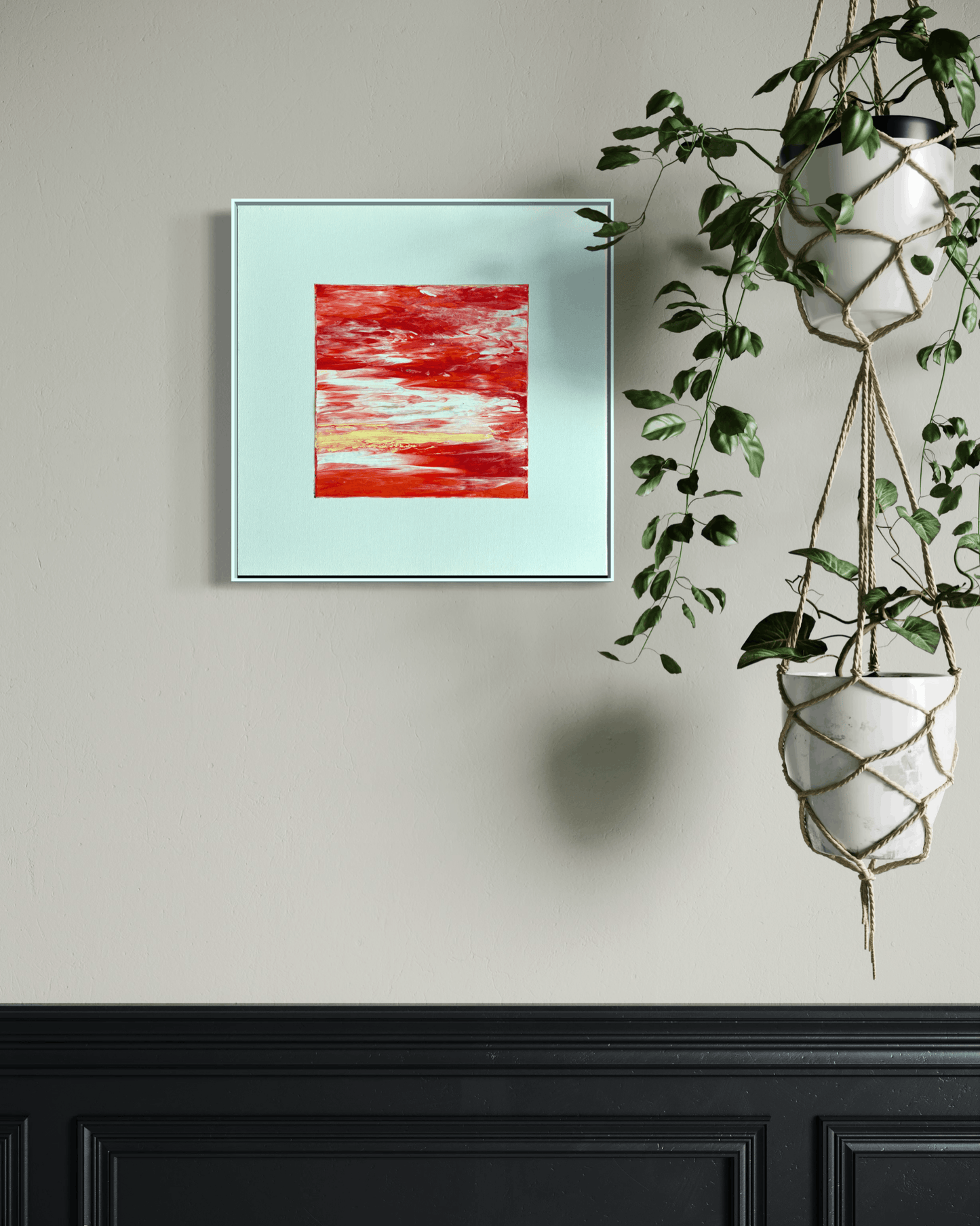 A framed abstract art print featuring a textured red and white composition on a pale mint background, displayed on a beige wall above a black wainscoted panel, with a hanging green plant to the right.