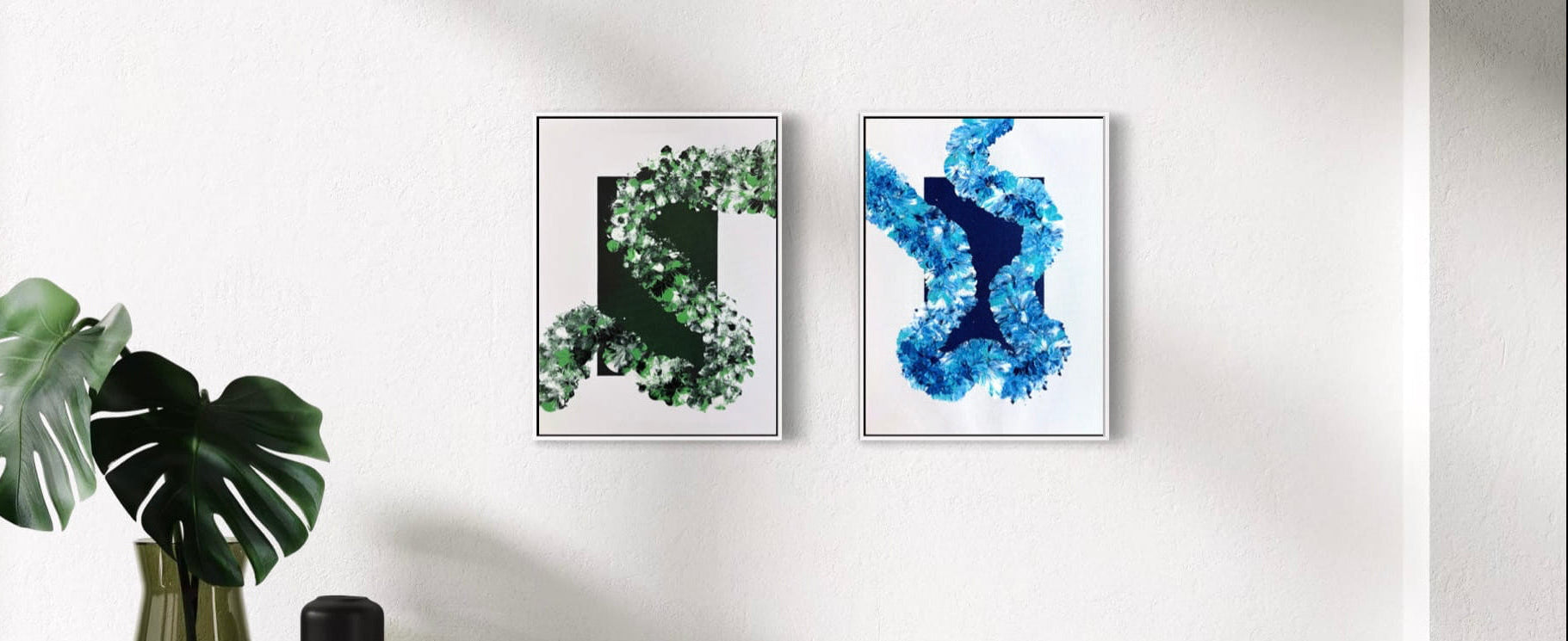 Two framed abstract wall art prints hang on a white wall in a modern interior setting. The left print features a green leafy spiral design, and the right print features an abstract blue and white pattern.