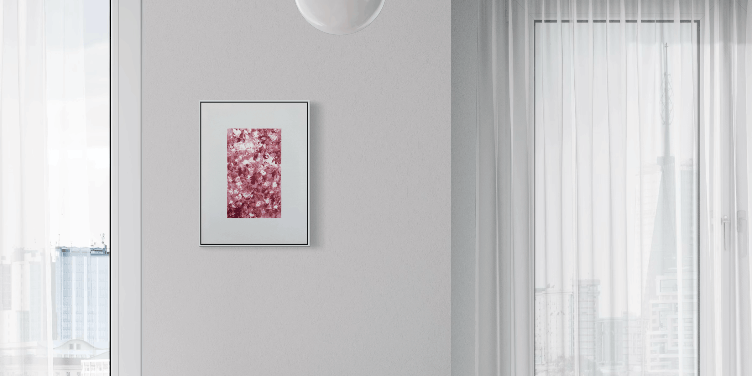 A framed abstract art print with pink and red floral-like patterns hangs on a light gray wall in a modern, sunlit room with sheer white curtains and a window view.